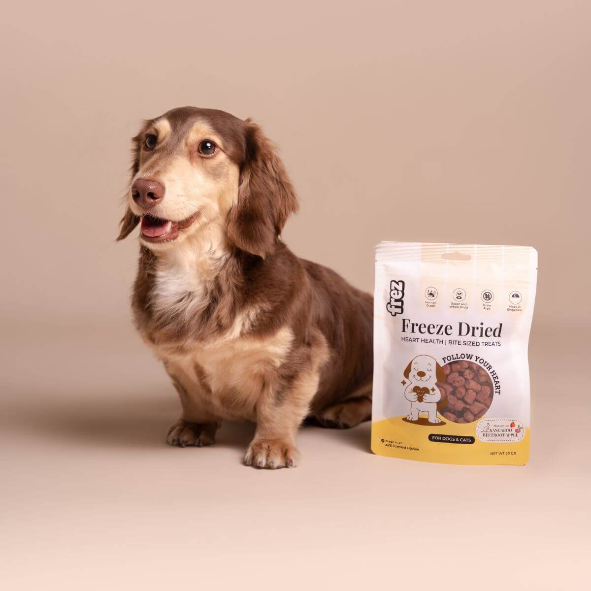 A dachshund standing beside the Frez Heart Health Freeze Dried Kangaroo with Beetroot & Apple Treats.