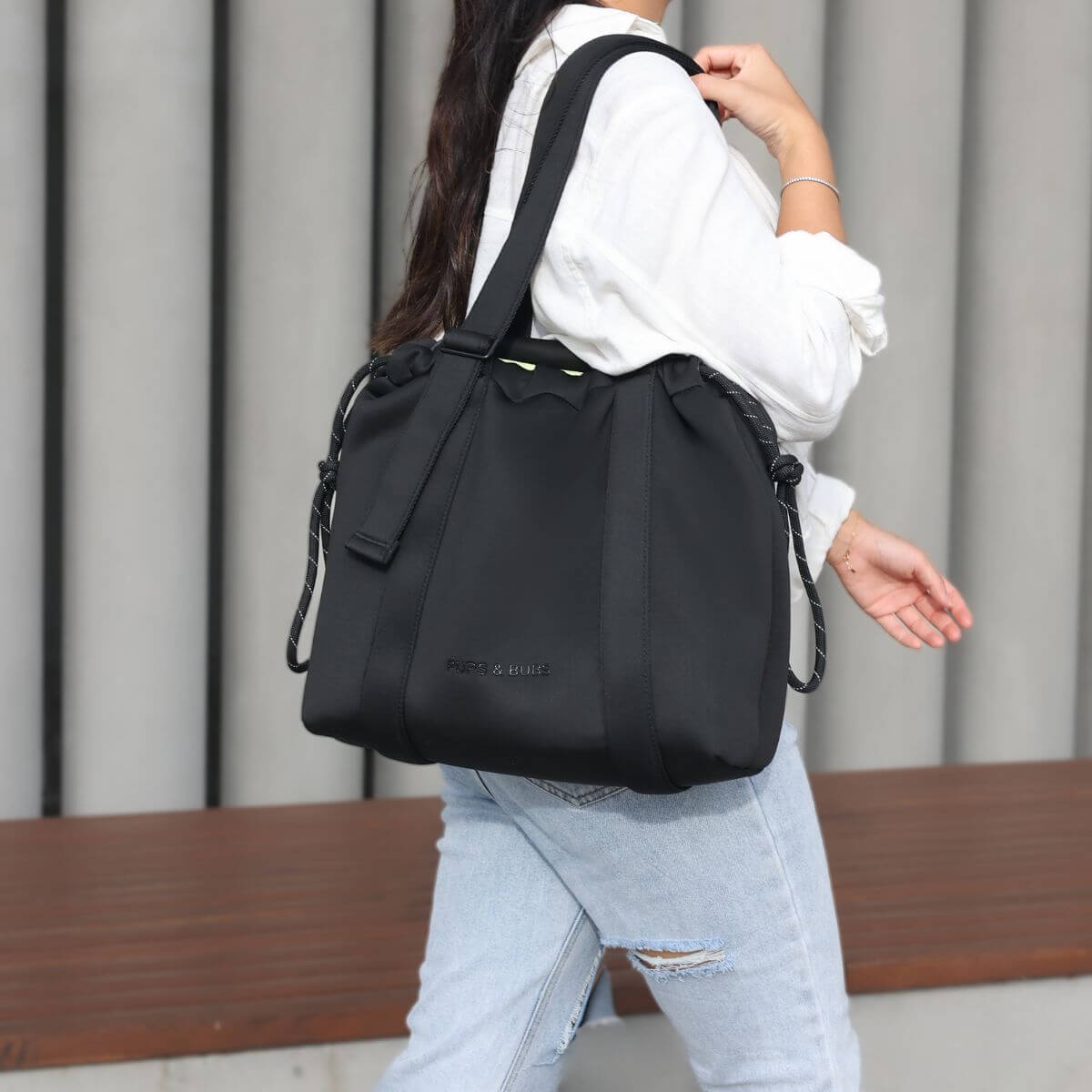 A woman carrying the Pups and Bubs All Day Chill Bag in Black on one shoulder outdoors.