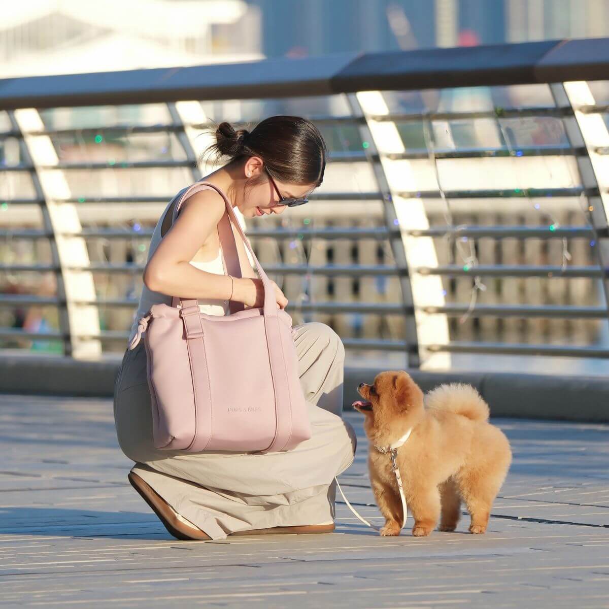 A woman carrying the Pups and Bubs All Day Chill Bag in Rose and a brown pomeranian.