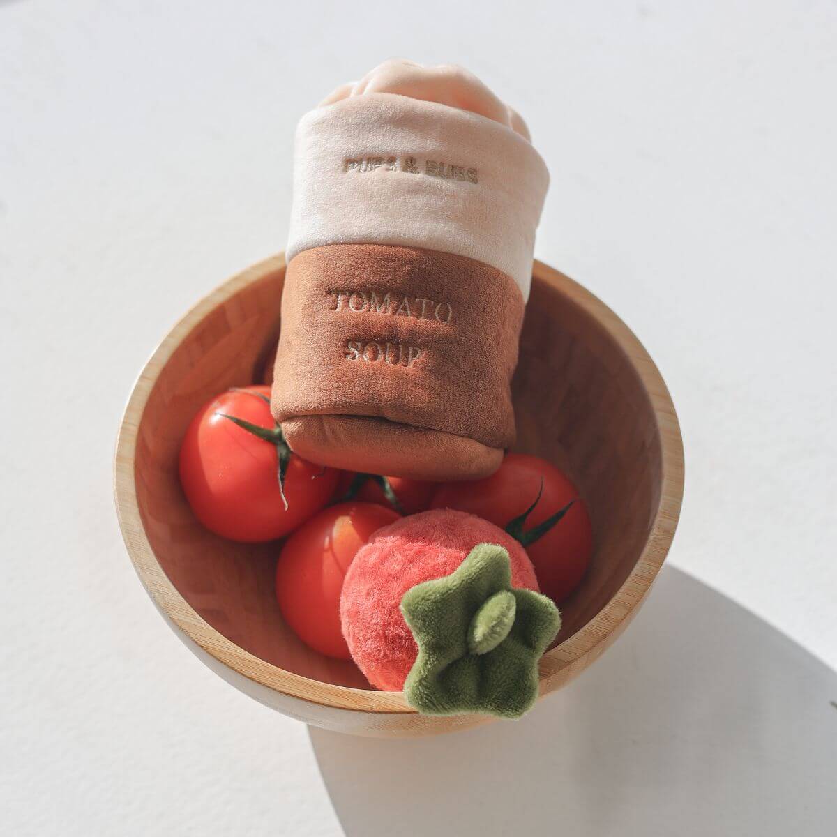 Pups and Bubs Tomato Soup Nosework Toy in a bowl with real tomatoes against a white table.