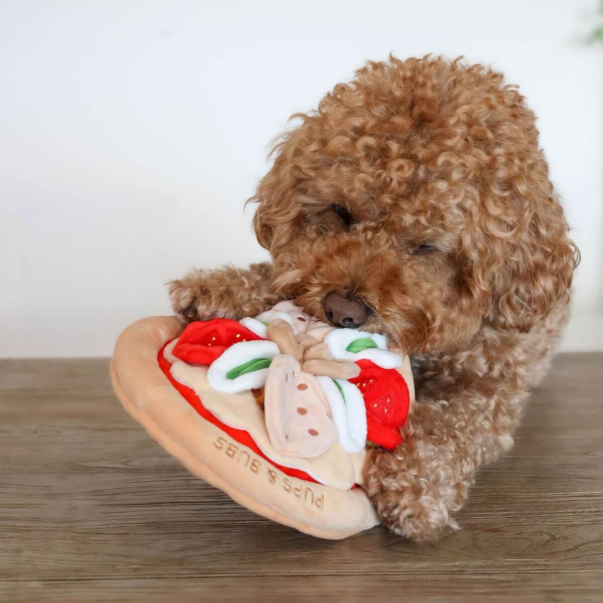 A brown poodle munching on the Pups & Bubs Pepperoni Pizza Snuffle Mat.