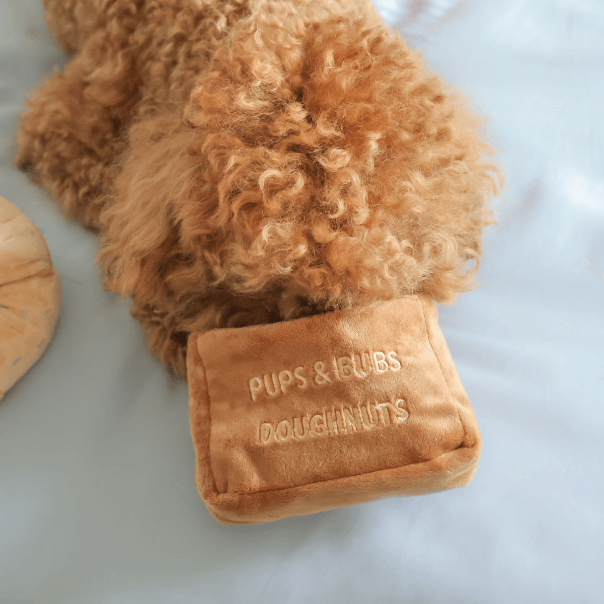 A brown poodle with its snout in the pups and bubs sprinkle donut nosework toy.