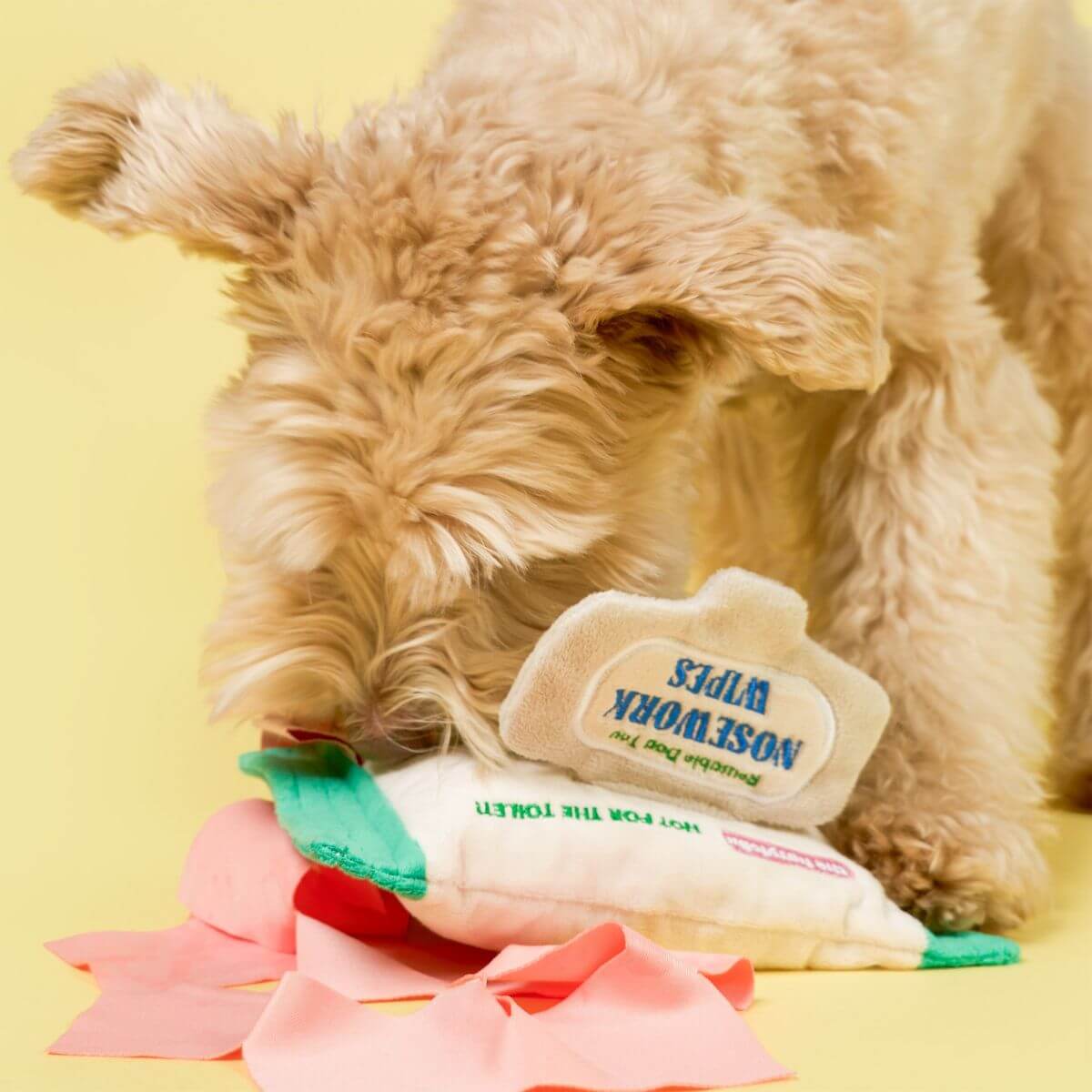 A dog snigging the the furryfolks doggo wipe nosework toy against a yellow background.
