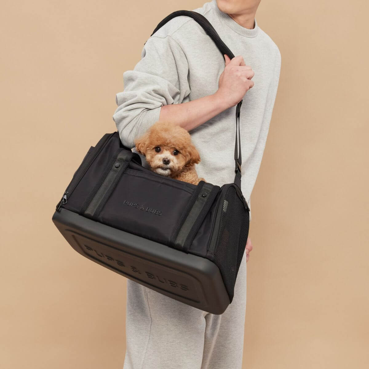 A dog peeking out of the top opening of the Pups and Bubs Onboard Travel Carrier  and slung over a man's shoulder.