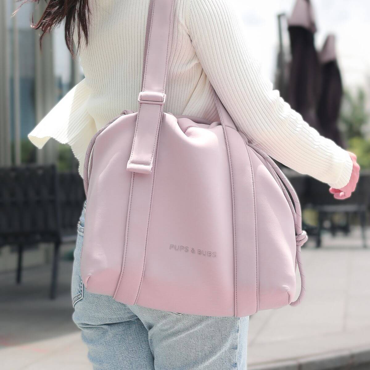 A woman wearing a white cardigan with a the Pups and Bubs All Day Chill Bag in Rose slung on the shoulders.