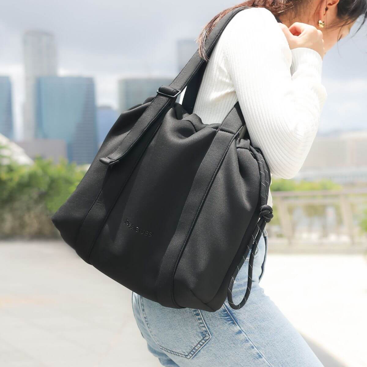 A woman carrying the Pups and Bubs All Day Chill Bag in Black on one shoulder outdoors.