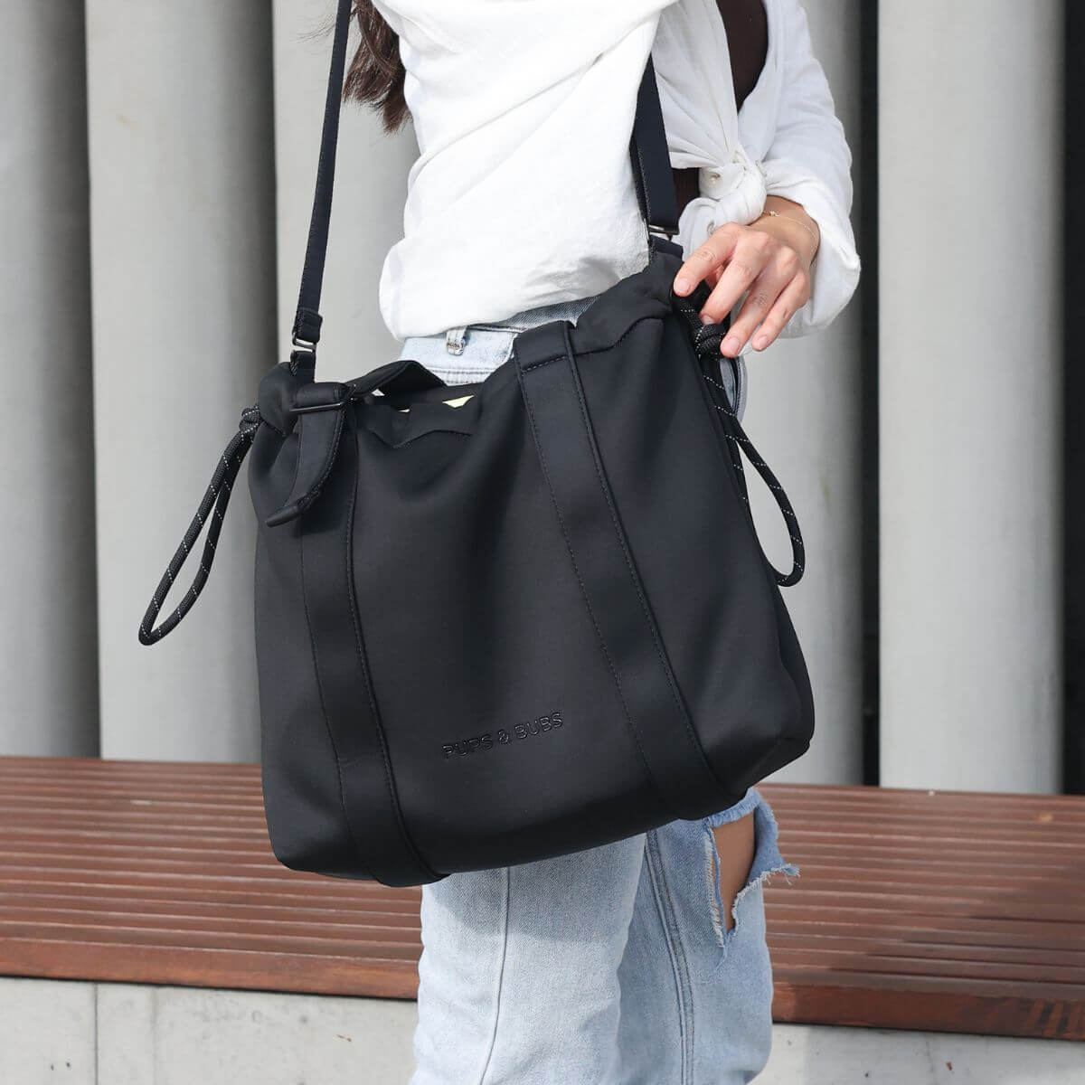 A woman wearing a white sweater carrying the Pups and Bubs All Day Chill Bag in Black as a crossbody.