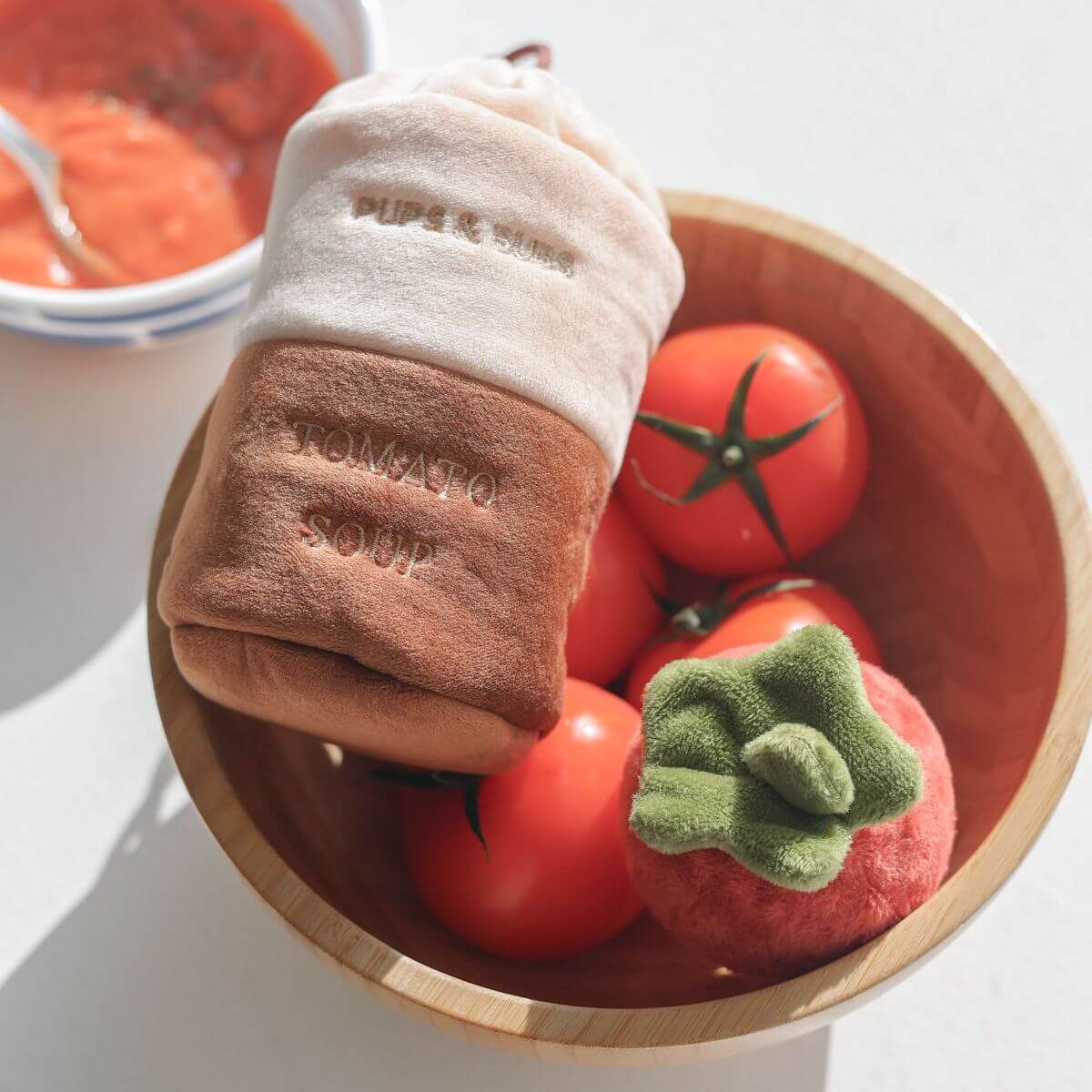 The Pups and Bubs Tomato Soup Nosework Toy in a bowl of real tomatoes on the tabletop. 
