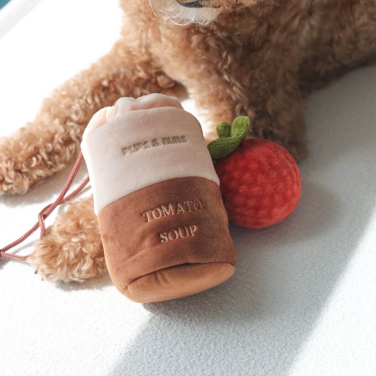Pups and Bubs Tomato Soup Nosework Toy with a brown poodle in the background.