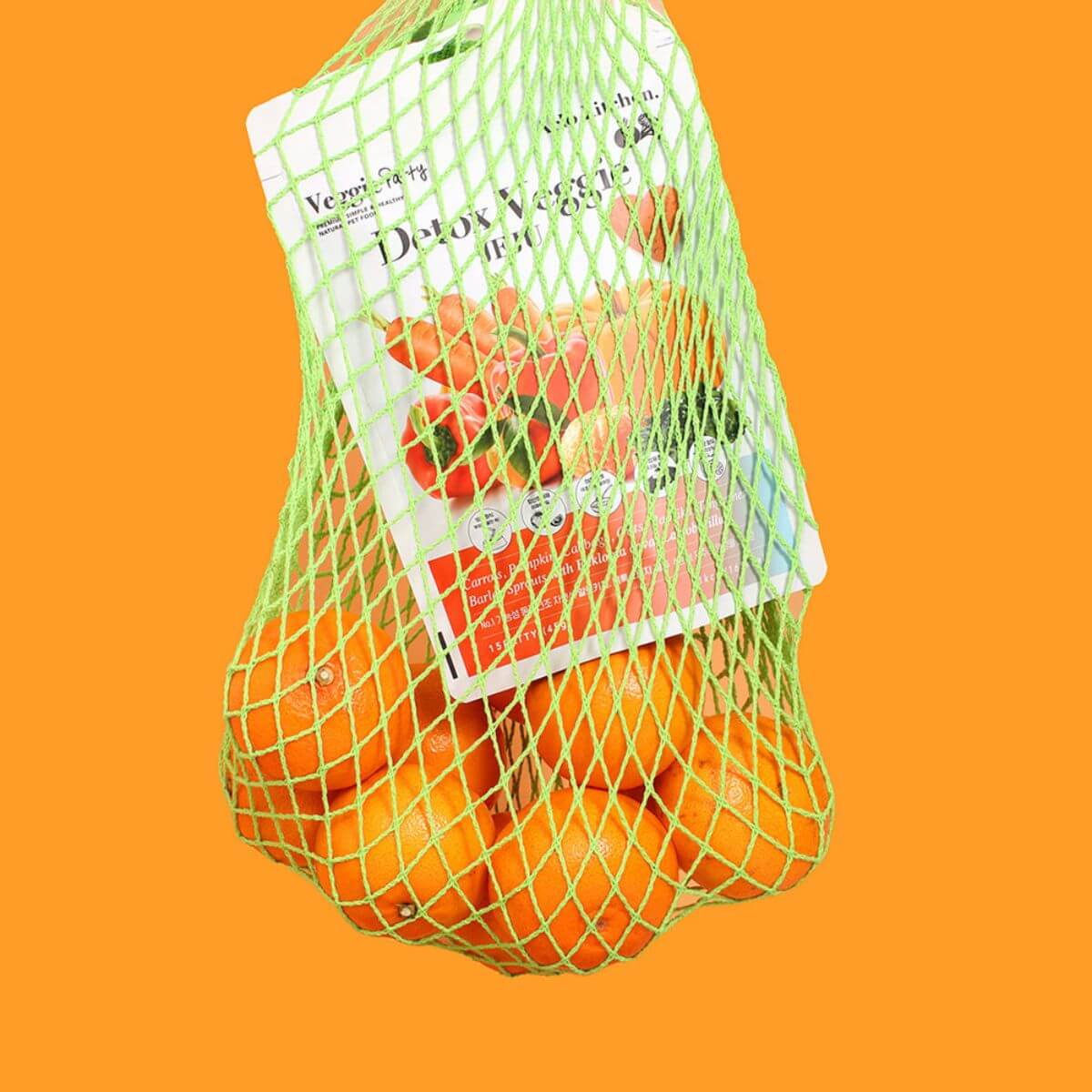 Arlo Kitchen Detox Veggie Jeju tangerines in a netted bag against an orange background.