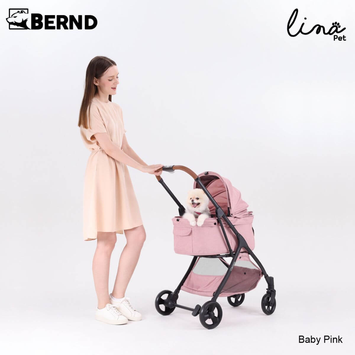 A woman pushing the Bernd Pets Autofold Lina in Baby Pink against a white background.