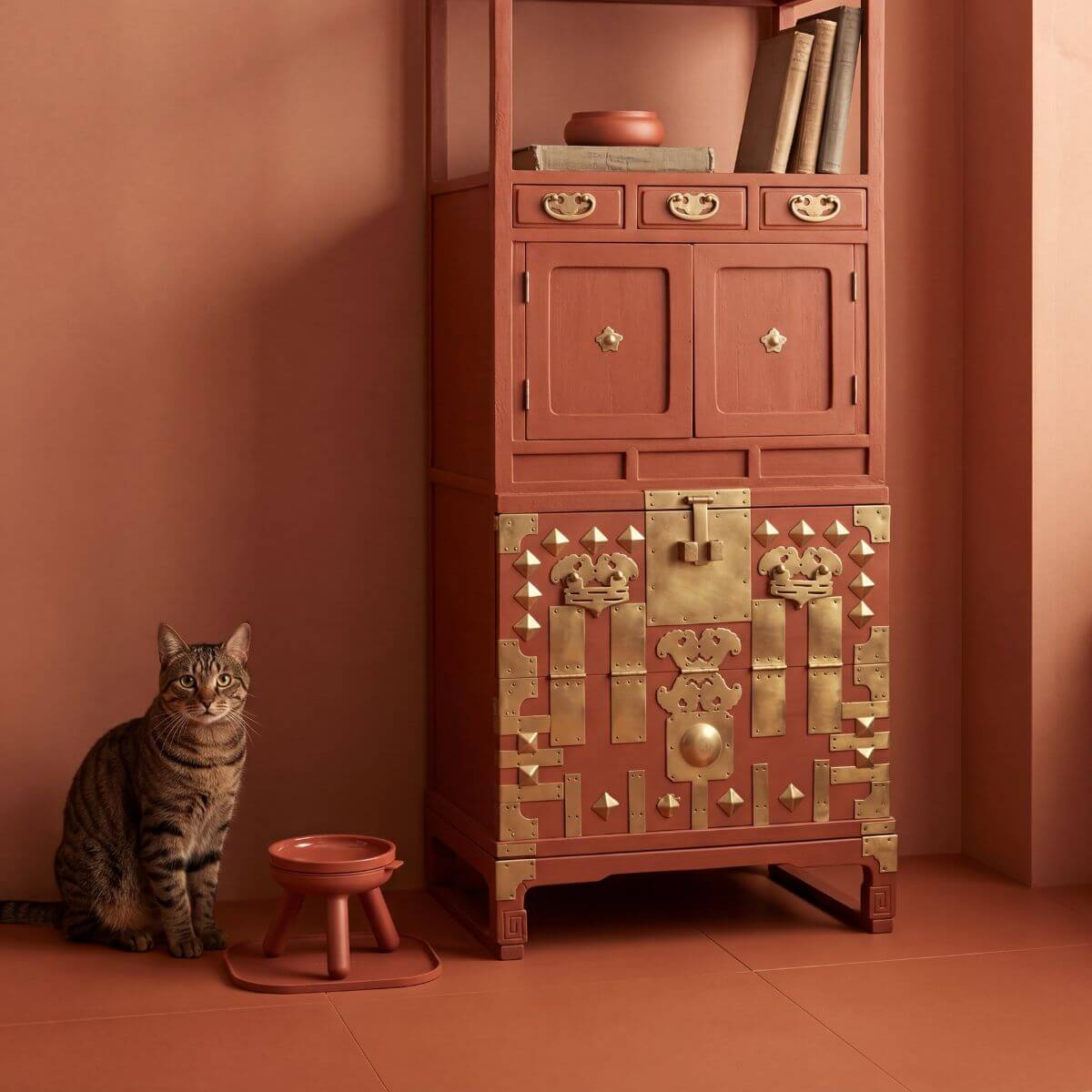 A cat with the inherent outdoor oreo table brick against a terracotta wall and an antique chest of drawers beside it.