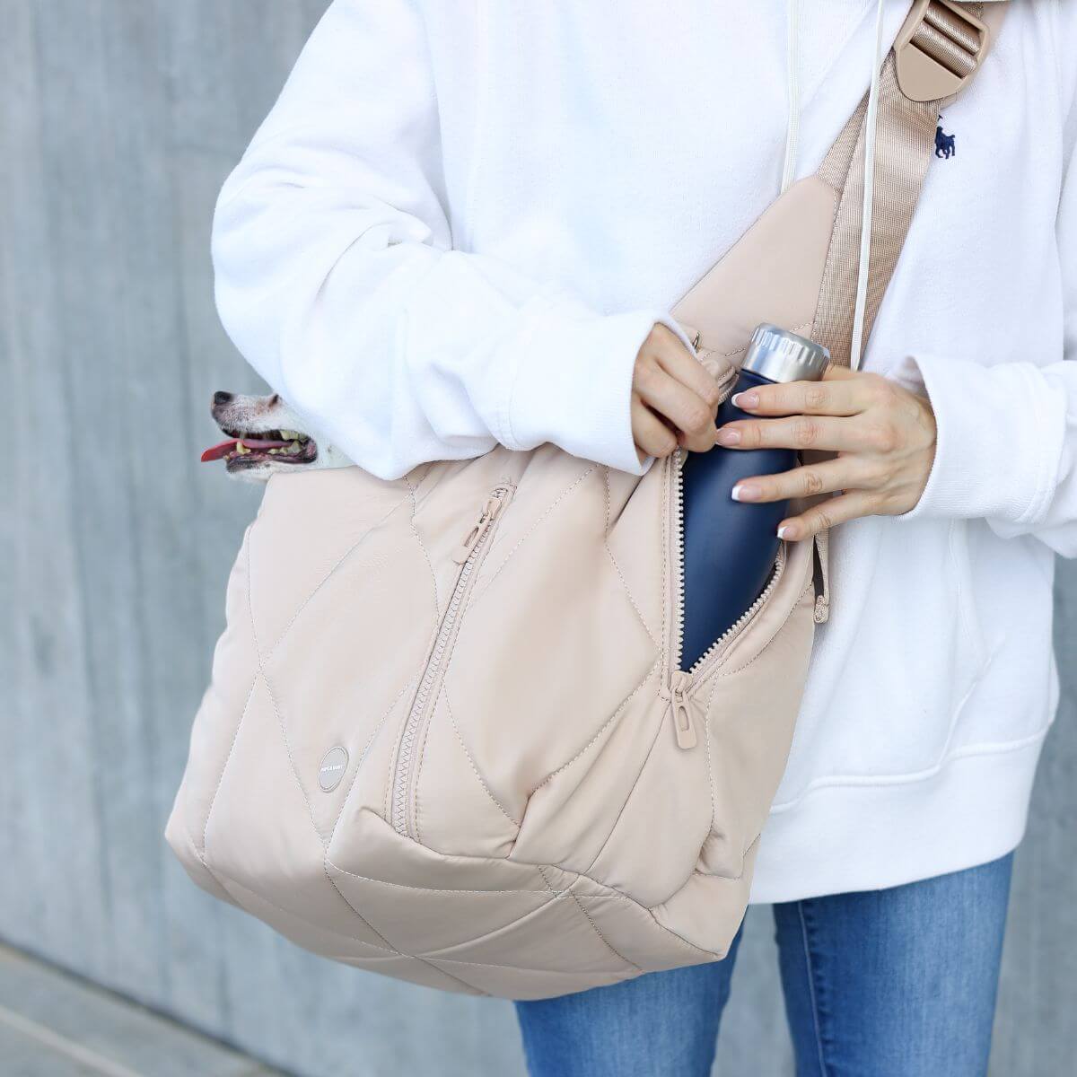 Pups & Bubs Cloud Crossbody Carrier in Latte and a bottle.