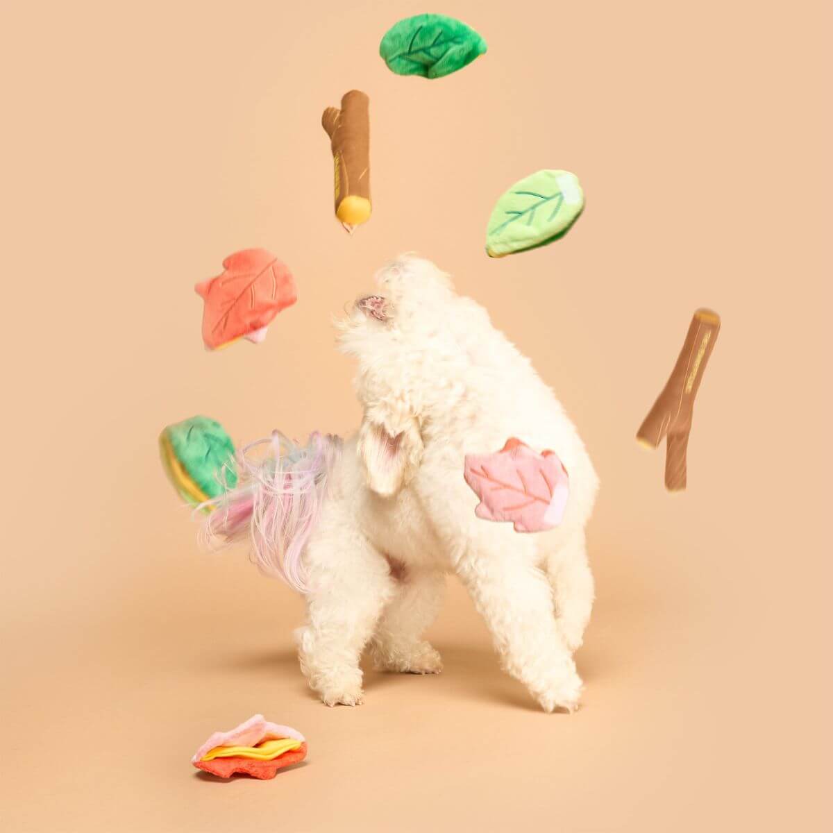 A dog and the deconstructed the furryfolks branch manager's branch nosework toy mid air against a beige backgroud.