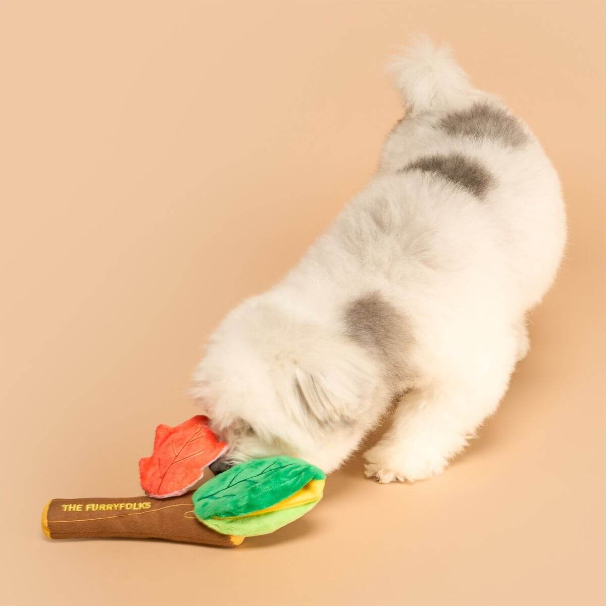 A dog sniffing the the furryfolks branch manager's branch nosework toy on the ground against a beige background.