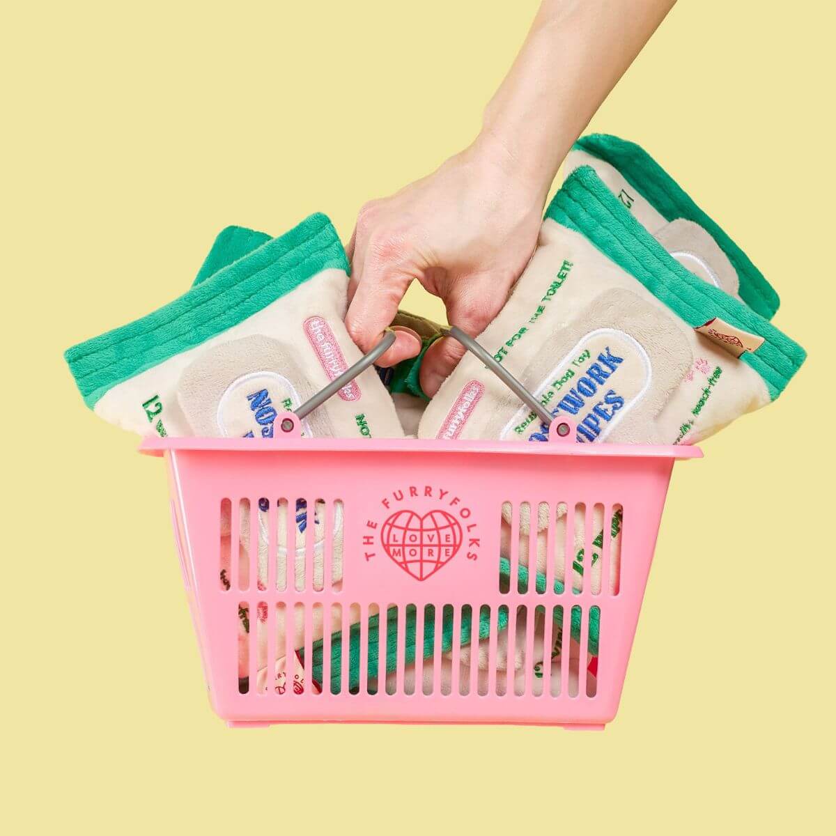 a the furryfolks pink basket that is filled with the the furryfolks doggo wipe nosework toy against a yellow background.